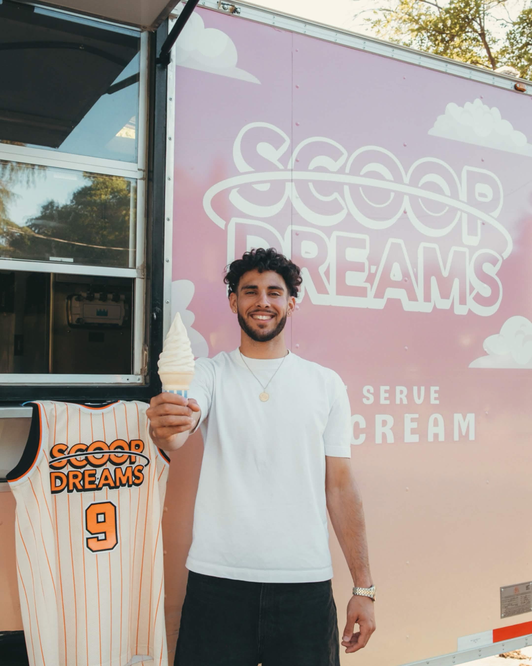 Devan Minouei holding a vanilla soft serve next to a hanging Scoop Dreams basketball jersey