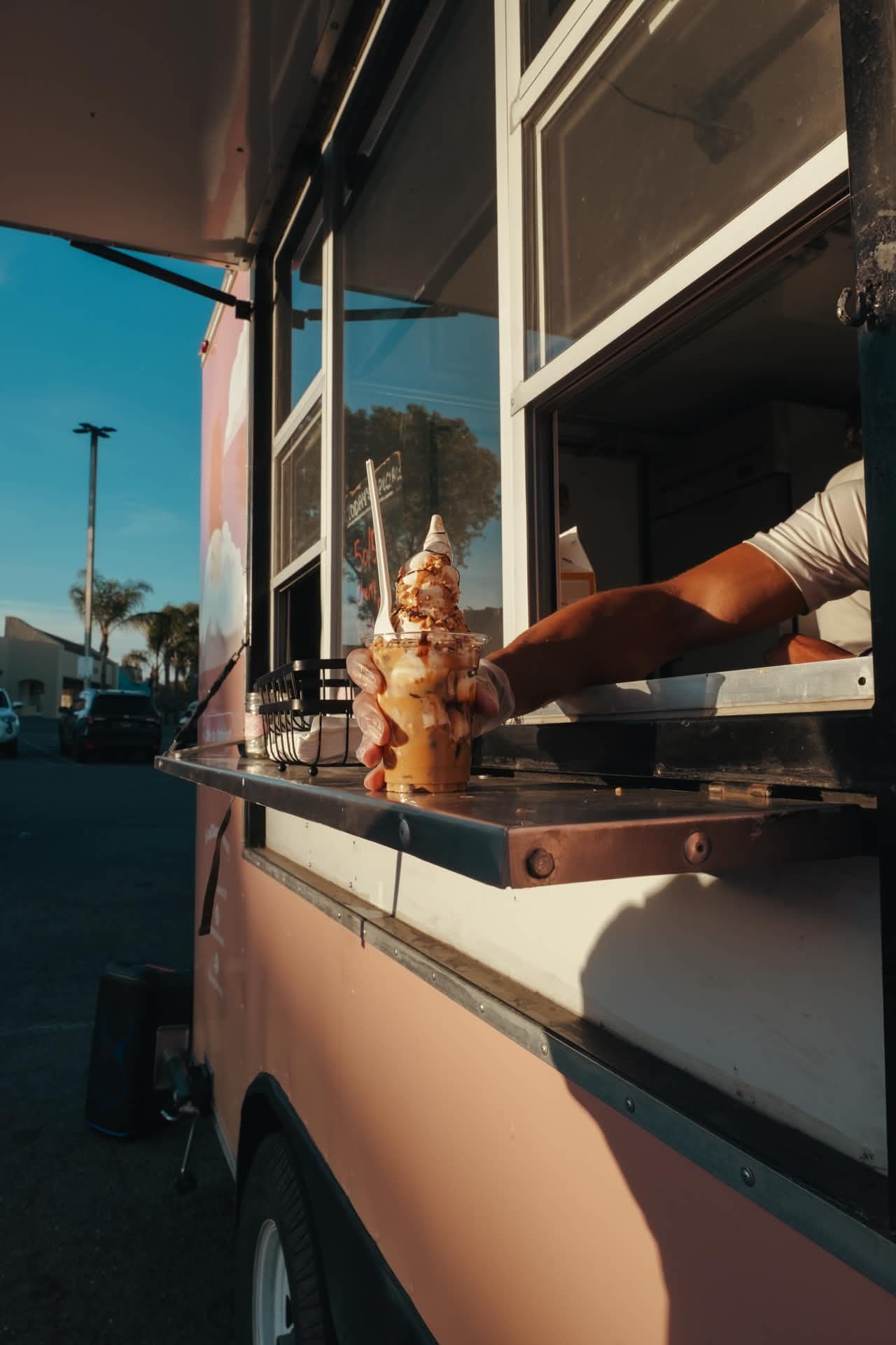A caramel sundae being handed through the Scoop Dreams trailer window at golden hour