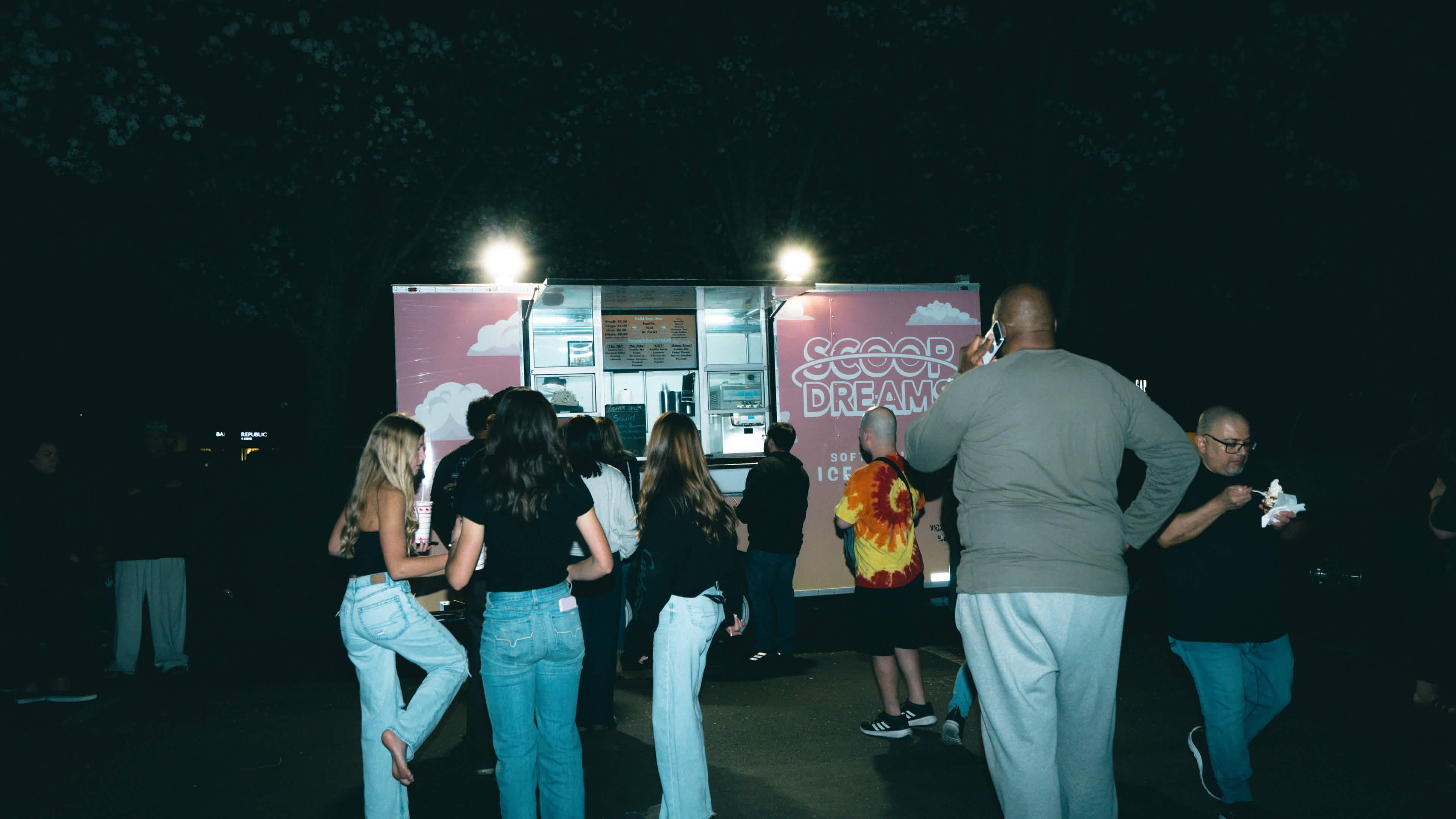A crowd ordering at the lit-up Scoop Dreams trailer at night
